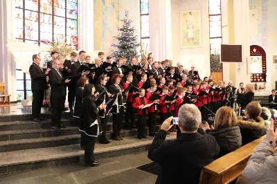 W niedzielę 26 stycznia 2025 r. w Katedrze Rzeszowskiej odbył się koncert kolęd w wykonaniu Katedralnego Chóru Chłopięco-Męskiego „Pueri Cantores Resovienses” pod dyrekcją Aleksandry Fiołek-Matuszewskiej. Tradycją chóru jest coroczne kolędowanie w Katedrze, więc nie mogło go zabraknąć także i w tym roku. Podczas koncertu wystąpiły gościnnie: Strzyżowski Chór Kameralny oraz Podkarpacki Chór Męski pod dyrekcją Grzegorza Oliwy. Koncert miał miejsce bezpośrednio po Mszy Świętej o godzinie 12:00, podczas której również zaśpiewał Katedralny Chór Chłopięco-Męski „Pueri Cantores Resovienses”. Po Eucharystii Rzeszowskie Słowiki pod dyrekcją Aleksandry Fiołek-Matuszewskiej dały piękny koncert. Na początku w wykonaniu połączonych chórów usłyszeliśmy kompozycję Dominika Lasoty „Przy wigilijnym stole”, po czym krótki rys historyczny Chóru i plan koncertu przedstawił Ryszard Bieniek – prezes Chóru. Dźwięki tak pięknych kolęd i piosenek świątecznych, jak: „Wśród nocnej ciszy”, „Carol of the bells” oraz „Jingle bells” wypełniły przestrzeń Katedry, wprowadzając zgromadzonych w świąteczny nastrój. Pięknie zabrzmiały również utwory: „Will we know him” oraz „Gdy Śliczna Panna” przy fortepianowym akompaniamencie Maksymiliana Rogóża. Następnie kolędowymi wykonaniami zachwycili słuchaczy zaproszeni goście. Podkarpacki Chór Męski wykonał kolędy: „Gore gwiazda”, „My też pastuszkowie”, „Lulajże Jezuniu”, „White Christmas”; a Strzyżowski Chór Kameralny zaprezentował pieśni: „Nad uśpioną Galileą”, „Kołysanka dla Jezusa”, „Dzisiaj w Betlejem” oraz „W dzień Bożego Narodzenia”. Dwie ostatnie kolędy zostały opracowane muzycznie przez Włodzimierza Korcza. Zarówno Podkarpackim Chórem Męskim jak i Strzyżowskim Chórem Kameralnym dyrygował Grzegorz Oliwa, który jest absolwentem Krakowskiej Akademii Muzycznej z tytułem profesora sztuk muzycznych. Prof. Grzegorz Oliwa był w latach 1988-1990 także chórzystą Katedralnego Chóru „Pueri Cantores Resovienses”. W kolejnej części koncertu męska część Chóru Pueri Cantores Resovienses, czyli tenory i basy, wykonała pod dyrekcją Aleksandry Fiołek-Matuszewskiej kolędy „W żłobie leży” oraz „Mizerna cicha”. Na zakończenie koncertu zabrzmiał jeszcze utwór „Powiadają aniołkowie”, który zgromadzona publiczność mogła usłyszeć w wykonaniu połączonych chórów męskich pod dyrekcją Grzegorza Oliwy. Po koncercie przyszedł czas na podsumowanie i podziękowania. Głos zabrał Ryszard Bieniek – wieloletni chórzysta i obecny prezes Katedralnego Chóru Chłopięco-Męskiego. Na zakończenie tego muzycznego wydarzenia zasłużeni artyści zostali uhonorowani kwiatami, a publiczność wyraziła swoją wdzięczność gromkimi brawami. Kolędę „Bóg się rodzi”, uważaną za królową wszystkich kolęd, połączone chóry wykonały wspólnie z publicznością, tworząc niezapomniane zakończenie tego spotkania. Podsumowując, koncert w Katedrze Rzeszowskiej był nie tylko muzycznym świętem, ale także wyjątkowym doświadczeniem duchowym, które zjednoczyło zgromadzonych w radosnym śpiewie i refleksji. Patronat nad koncertem objął bp Jan Wątroba. Do zobaczenia na następnych koncertach! ks. Julian Wybraniec fot. Patrycja Pelczar Reszko